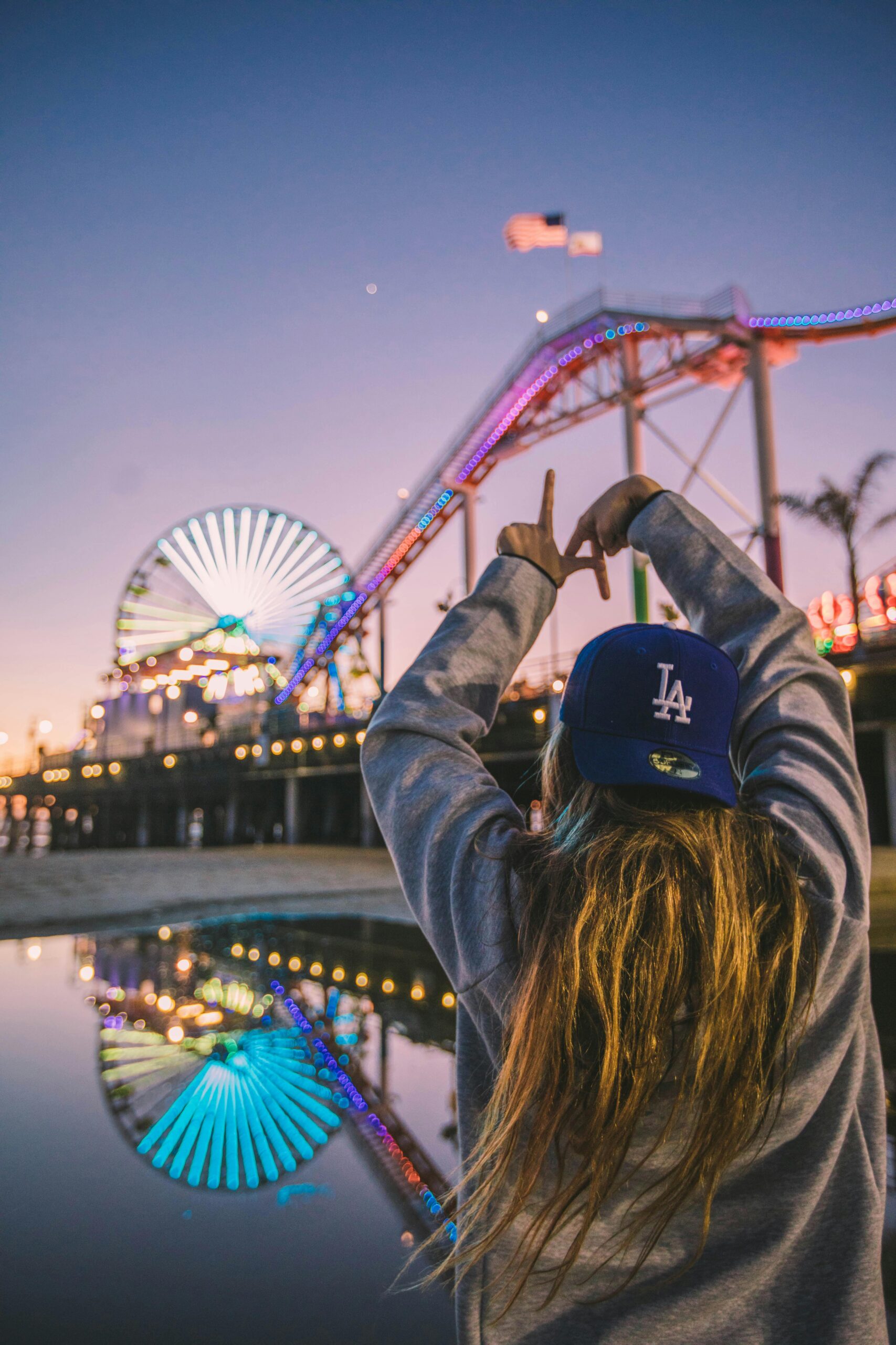 Back view of a woman enjoying Santa Monica Pier amusement park at twilight, reflecting vibrant lights.